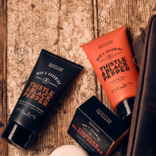 Thistle & Black Pepper Face & Beard Wash with shaving products on a wooden surface