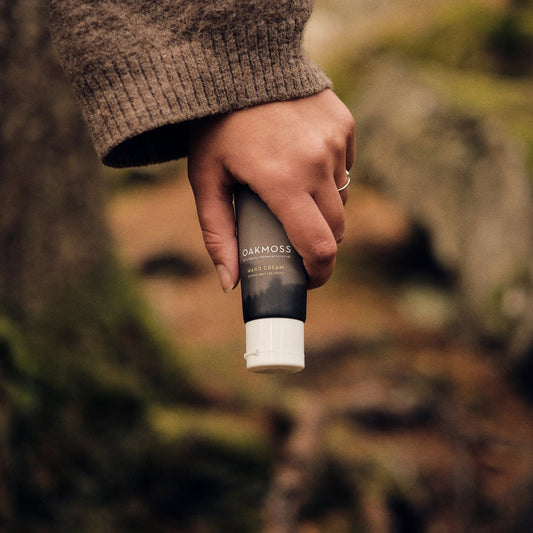 Hand holding an Oakmoss Hand Cream tube in a woodland setting