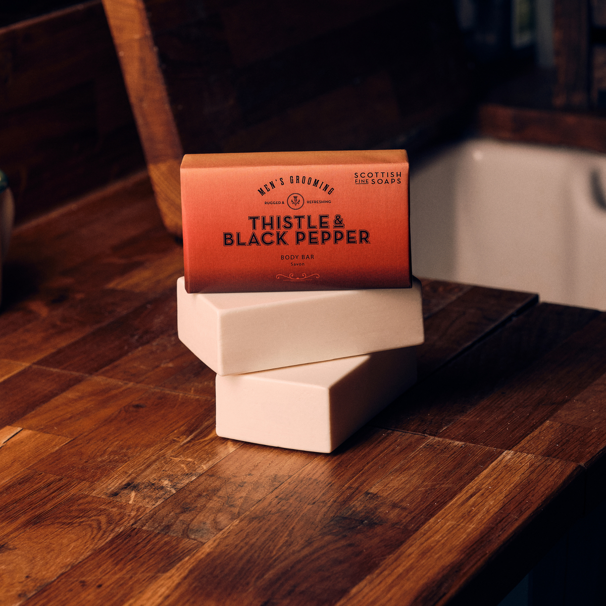 Boxed Thistle & Black Pepper Body Bar with unwrapped white soap bars on a wooden surface
