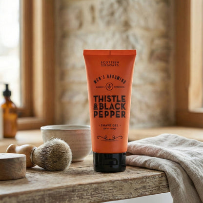 Orange Thistle & Black Pepper Shave Gel tube beside a towel and shaving brush