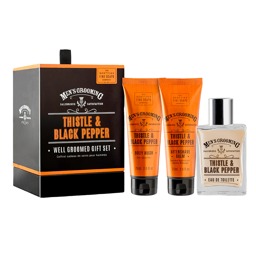 The Scottish Fine Soaps Company Men’s Grooming Well Groomed Gift Set featuring a black and orange box with Thistle & Black Pepper branding, alongside three grooming products: a 50ml Eau de Toilette, a 75ml Aftershave Balm, and a 75ml Body Wash in matching orange packaging.