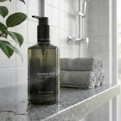Oakmoss Body Wash pump bottle beside folded towels on a stone bathroom ledge