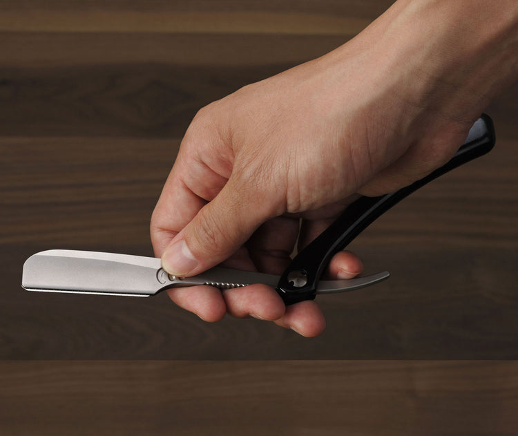 Hand holding a straight razor on a wooden background