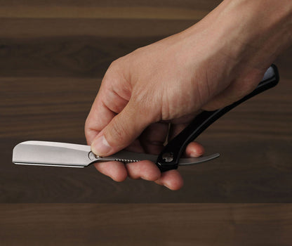 Hand holding a straight razor on a wooden background