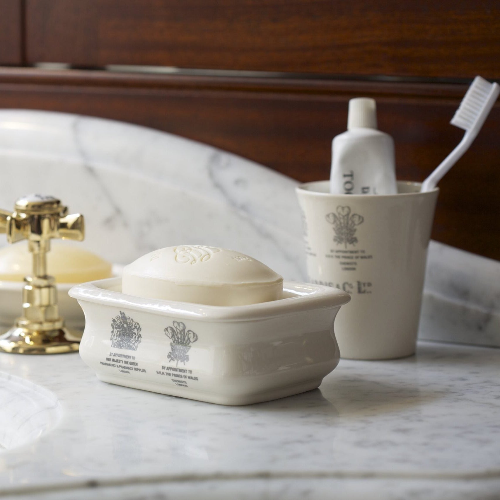 Bathroom sink with gold faucet, soap dish, and toiletries on a marble countertop.