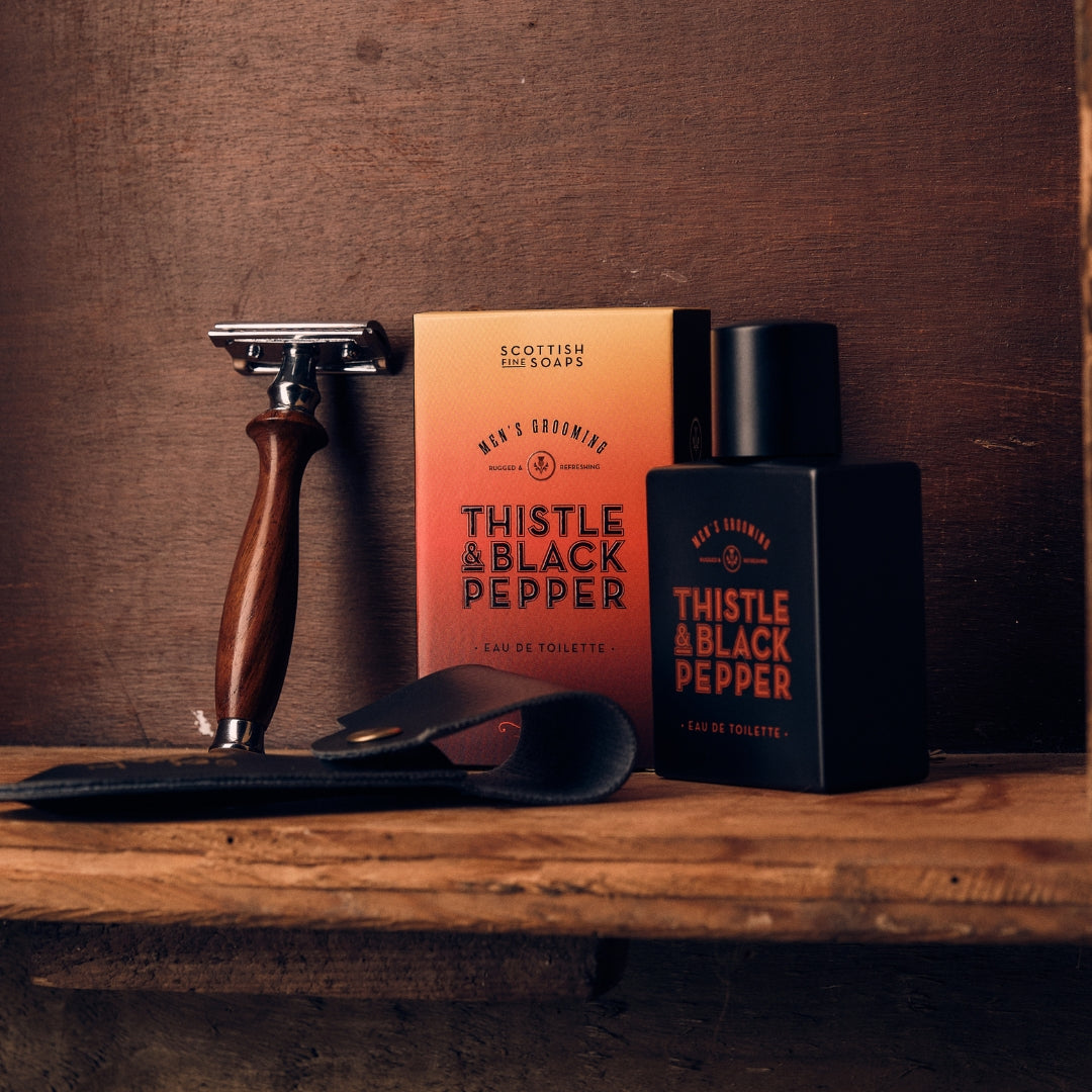 Thistle & Black Pepper Eau de Toilette with its box and a razor on a wooden shelf