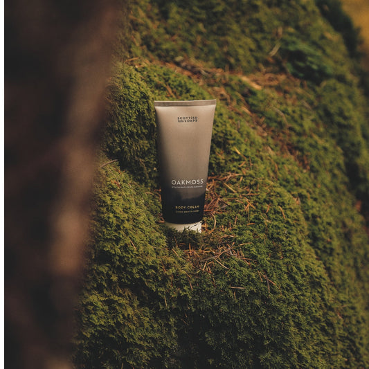 Oakmoss Body Cream tube resting against a moss-covered tree