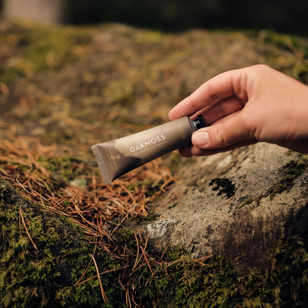 Hand holding an Oakmoss Hand Cream tube over moss and tree roots