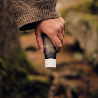 Hand holding an Oakmoss Hand Cream tube in a woodland setting