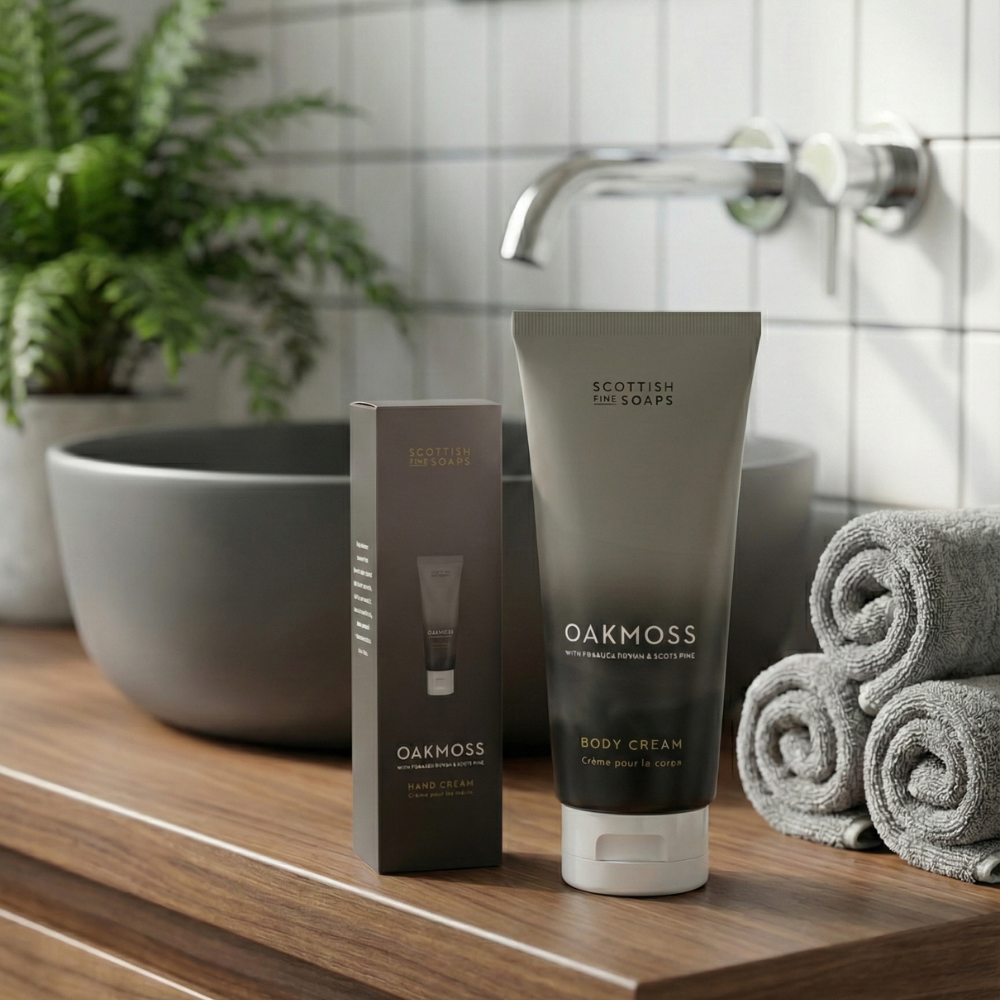 Oakmoss body wash and cream tubes with rolled towels beside a bathroom basin