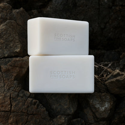 Two unwrapped Thistle & Black Pepper soap bars resting against textured bark