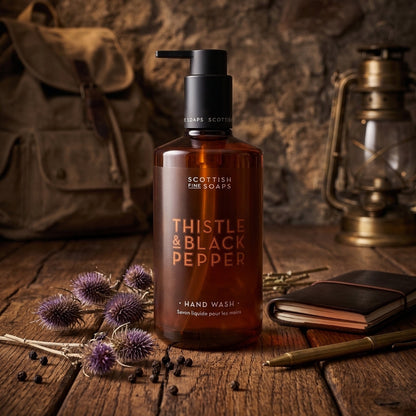 Thistle & Black Pepper Hand Wash pump bottle on wood beside thistles and grooming accessories