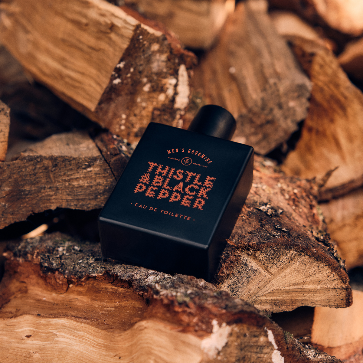 Thistle & Black Pepper Eau de Toilette bottle resting on stacked firewood