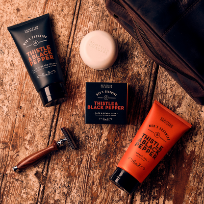 Thistle & Black Pepper Shave Gel with face wash and shaving soap on a wooden surface